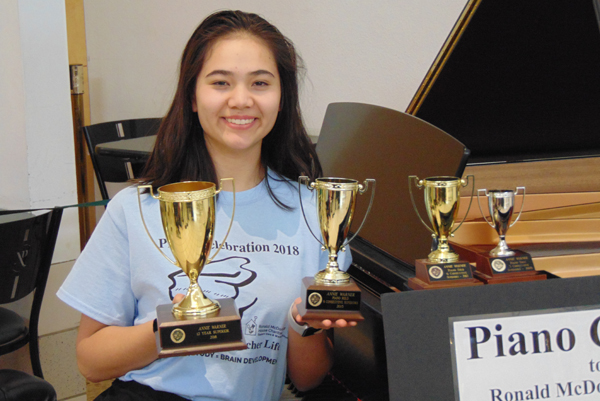 girl holding trophies while sitting at piano
